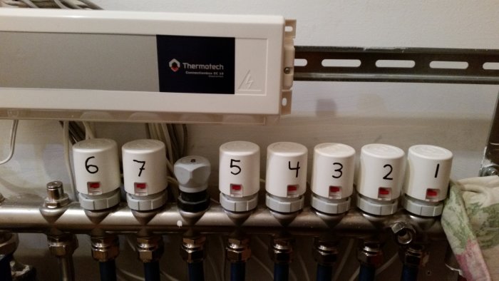 Thermotech golvvärmesystem med vit fördelningslist och justerbara ventiler märkta 1 till 8, en ventil är vriden på max.