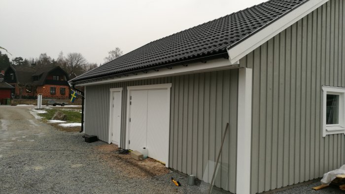 Husfasad med nyinstallerad takavvattning och vita dörrar; grindstolpar syns i förgrunden utan påsatthuvar.