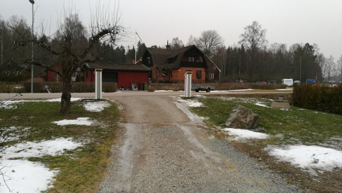 Uppfart till en trävilla med nyinstallerad takavvattning och nybyggda grindstolpar utan plåthuv.