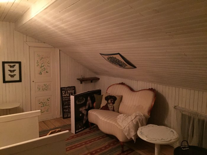 Gammaldags inredd vind med lutande tak, vit soffa, konst och texttavlor.