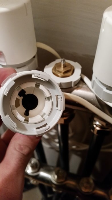 Hand håller en vit termostatknopp framför en radiatorventil, den svarta delen syns stillastående inuti.