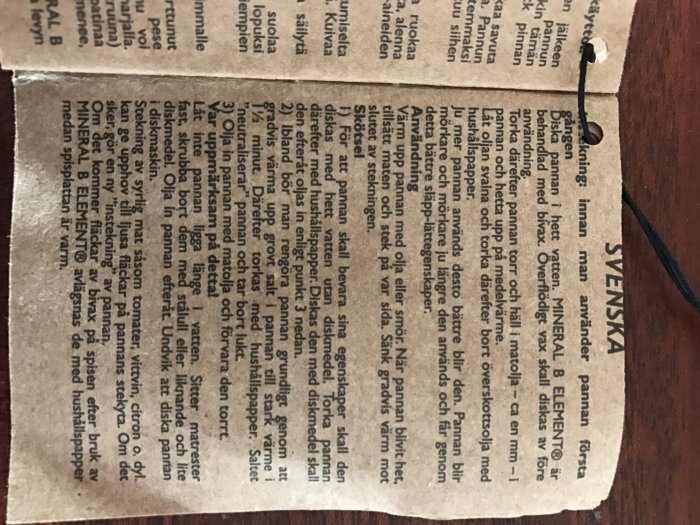 En öppen instruktionsbok med text på svenska ligger på ett mörkt underlag, med synlig text som ger råd om användning av 'medelvärme'.