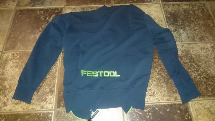 Marinblå tröja med Festool-logotyp placerad på ett kakelgolv.