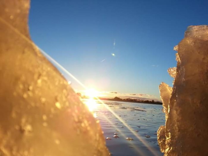 Solnedgång sedd genom isblock vid Vikbolandet, reflektioner på vattnet.