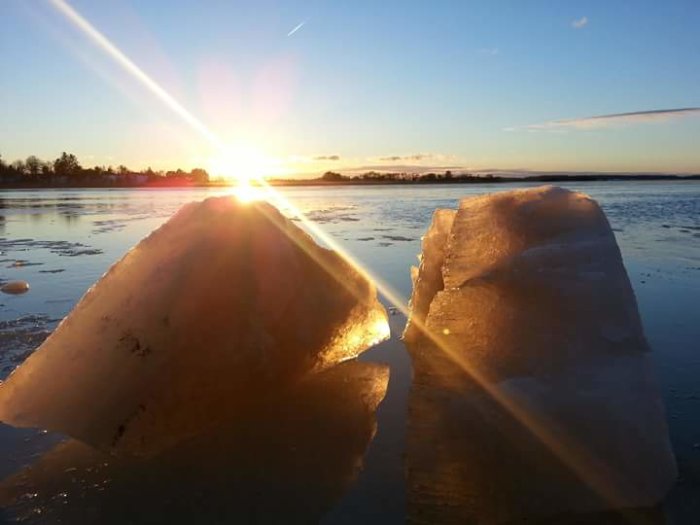 Solnedgång bakom isblock vid fruset vatten på Vikbolandet, ljusstrålar i bild.