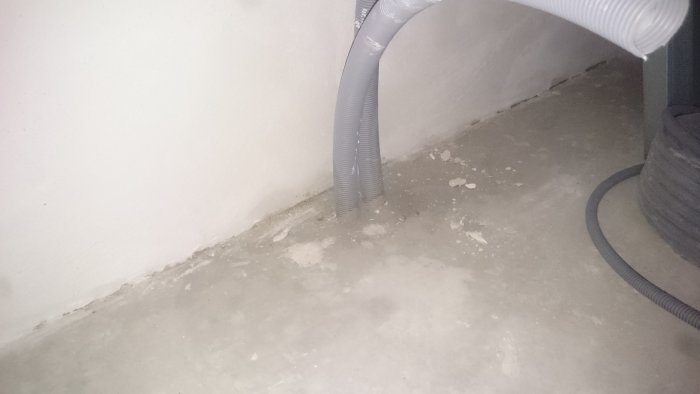 PEX-rör som kommer upp ur ett betonggolv i ett hörn innan klinkers är lagt, omgivet av väggar och ett flexibelt rör.