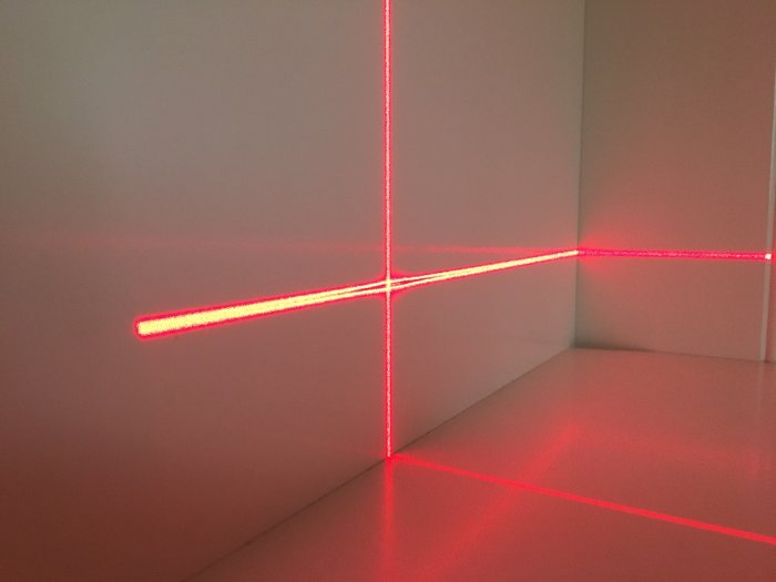 Krysslaserprojektion från Bosch GLL 2-10 med otydlig linje i mitten på en vit vägg och golv.