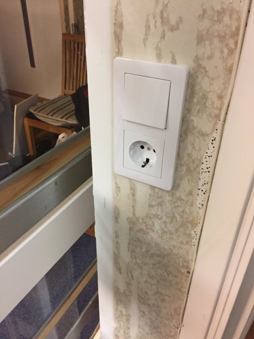 Nyinstallerad vit vägguttag med jordfelsbrytare bredvid en skjutdörr under renovering.