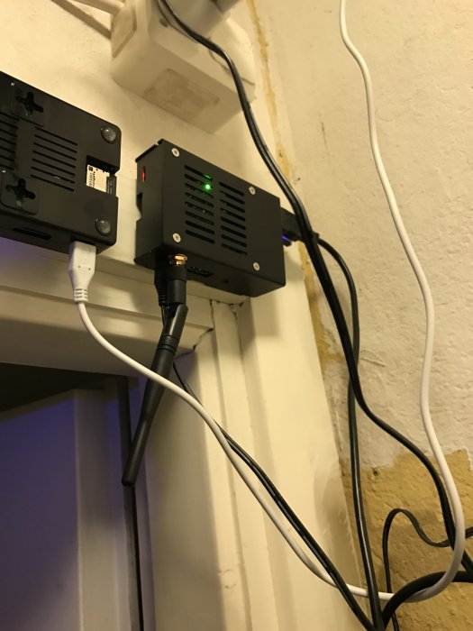 Monterad extern antenn på Raspberry Pi med plåthölje vid en vägg, kablar och en strömadapter synliga.