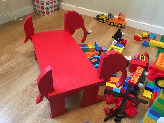 Handgjord röd elefantpall på ett golv omringad av leksaksbilar och legobitar.