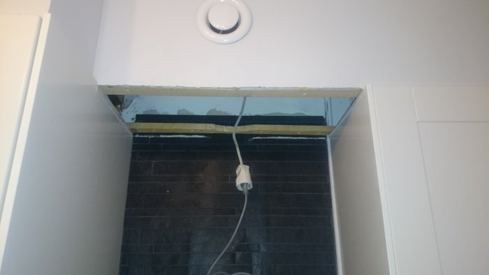 Underliggare med osläckt kabel och öppet hål i taket ovanför svart kakelvägg.