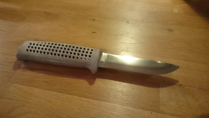3D-printad kniv med titanhandtag och nyslipat blad liggande på ett träbord.