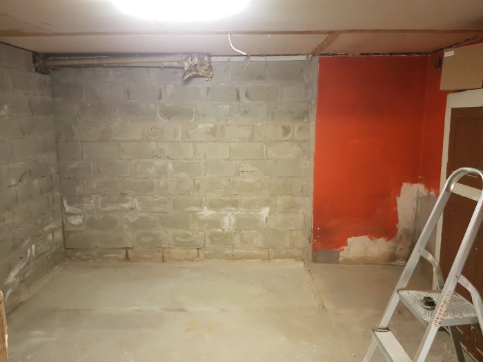 En orenoverad källare med nakna betongväggar, en röd målad sektion och rör längs taket.