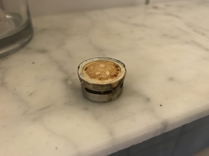 Rostig strålsamlare från tvättställsblandare på marmorbänk.