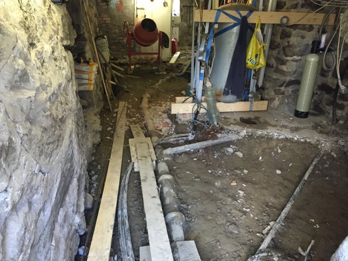 Undergång av källarrenovering med uppbrutet golv, armeringsarbeten och synlig naturstensgrund.