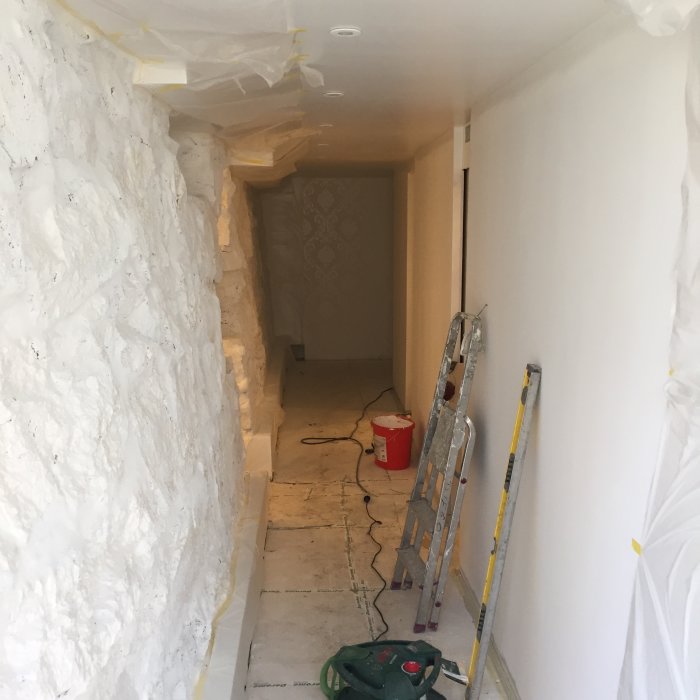 Renoveringsprocess i källargång med vita målade stödmurar och golv under arbete.
