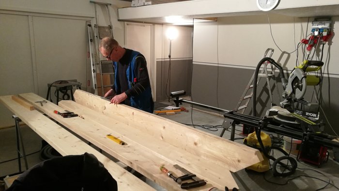 Man arbetar med trämaterial för trappa i verkstad med verktyg och såg.