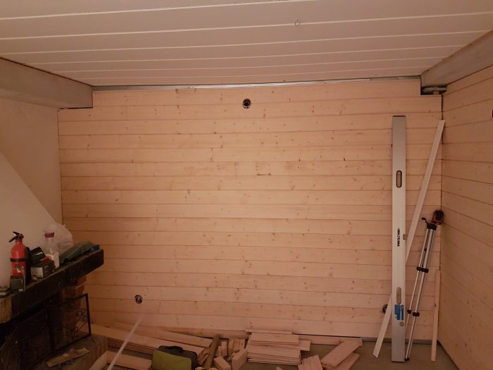 Interiör av ett rum under renovering med träpanel på väggar och byggmaterial på golvet.