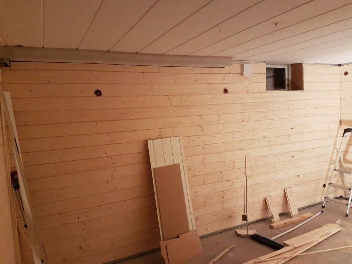 Träpanelbeklädnad på väggar i ett pågående inomhus renoveringsprojekt med byggmaterial synligt.