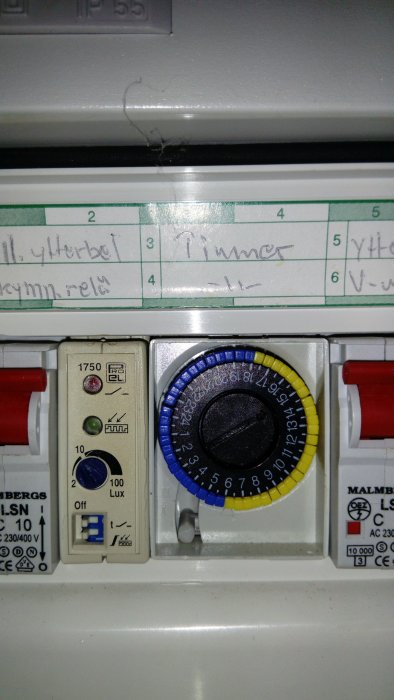 Timer med inställningsratt och skymningssensor för utebelysning, handskrivna etiketter ovanför.