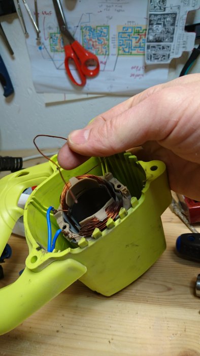 En hand håller öppet ett elverktyg med synliga koppartrådar och komponenter inuti.