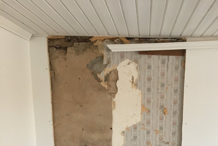 Delvis avlägsnat väggmaterial framför murstock, exponerande gammal puts och tegelstenar.