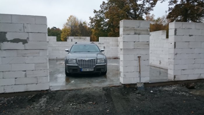 Bil parkerad framför en oavslutad garagebyggnad av betongblock under uppförande.