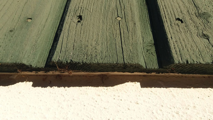 Närbild på en laserad träpanel på ett hus, visar tecken på åldring och slitage.