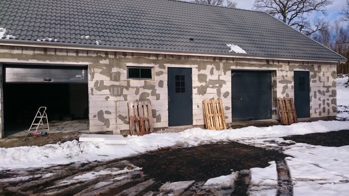 Garage under konstruktion med putsad fasad, två portar, en dörr och snörest på taket.