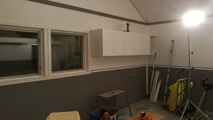 Nyinstallerat väggskåp ovanför arbetsbänk i renoverad toavägg med målarutrustning och verktyg synliga.