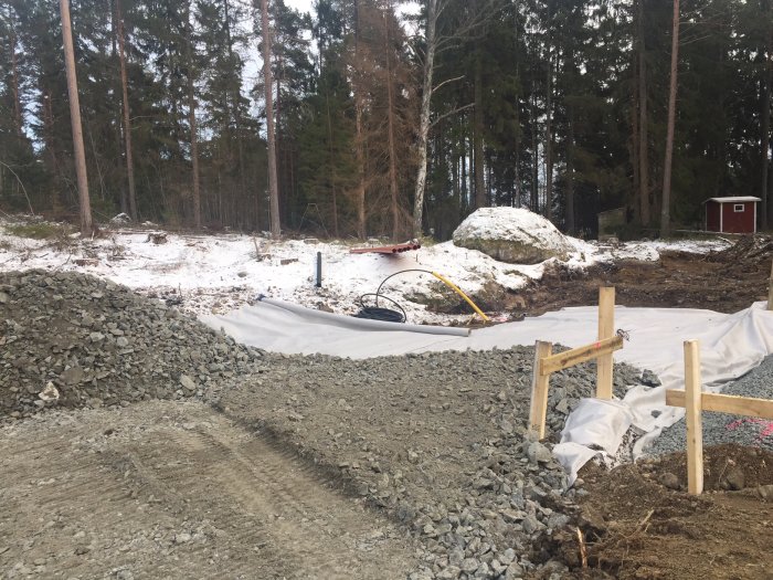 Grusad mark med förberedelser inför betongplatta, träd i bakgrunden och plats för carport.