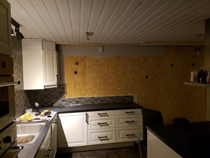 Påbörjat köksrenovering med borttagna överskåp och vitvaror, OSB-skivor på väggen.