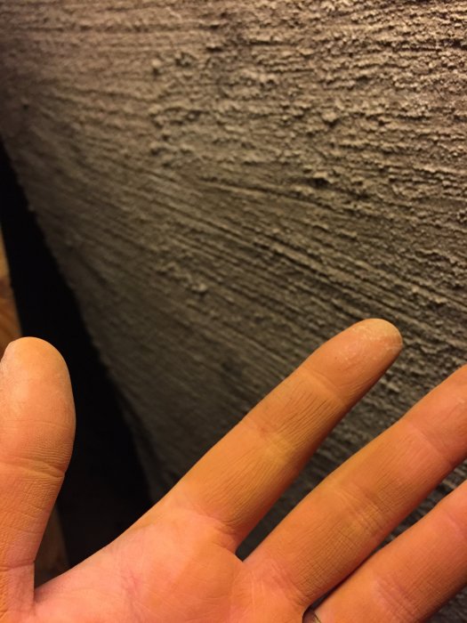 Närbild på en hand framför grov, våt lera som möjligen är utfällt järn.