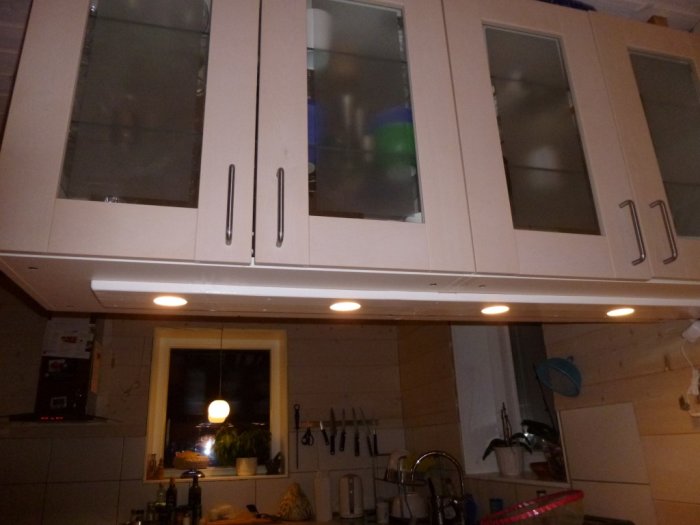 Vit köksöverkåp med glasdörrar över en kökshalvö, skapar avskiljning mot matplats.