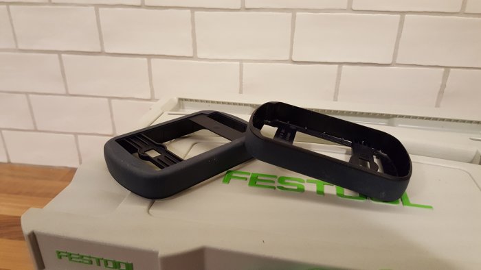 Två svarta plastdelar förmodligen tillbehör till Festool verktyg på vit Festool låda.