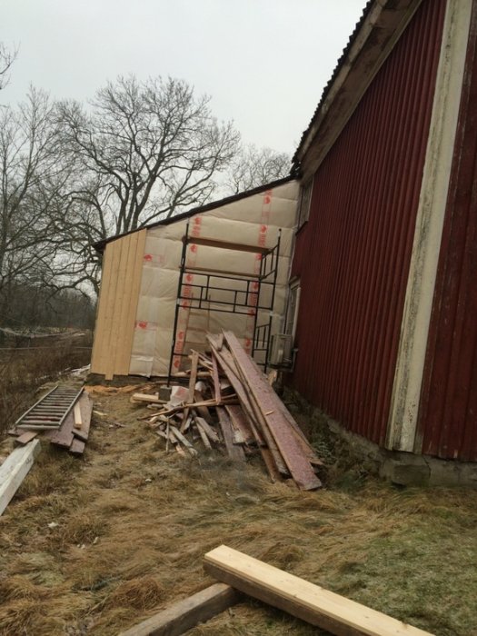 Pågående isoleringsarbete på yttre vägg av röd gammal lada, med isoleringsmaterial och byggställning.