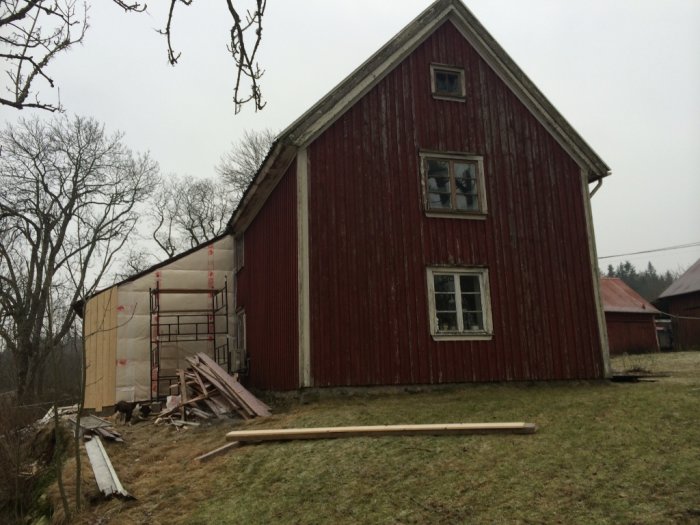 1700-talshus med rött träfasad och vita fönster under renovering med byggställning och träplankor på marken.