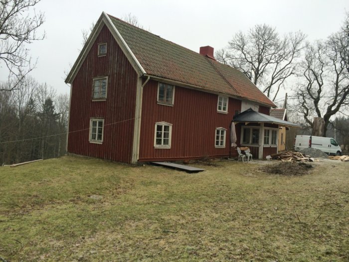 Rödmålat, tvåvånings 1700-talshus med tegeltak, under renovering med byggmaterial utspritt framför huset.