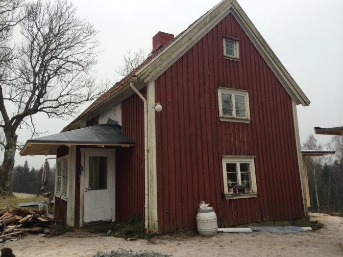 Rödmålat 1700-tals hus i två våningar med vita fönsterfoder och plåttak, omgivet av träd och viss snö.