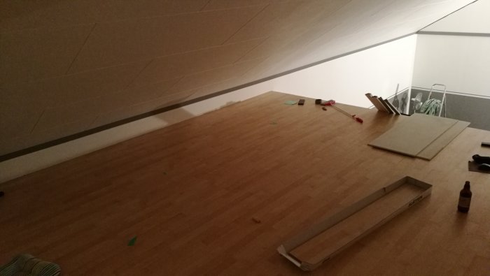 Nylagt trägolv på loft med verktyg och trappa under lutande tak, redo att målas.