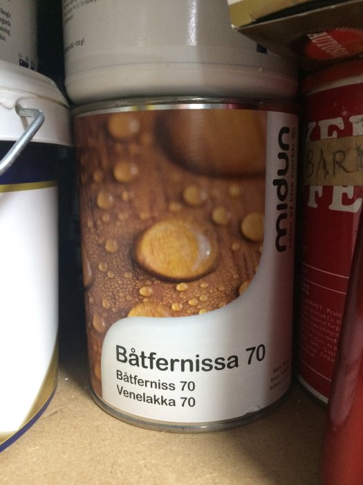 Burk med båtlack märkt "Båtfernissa 70" i en hylla omgiven av andra burkar.