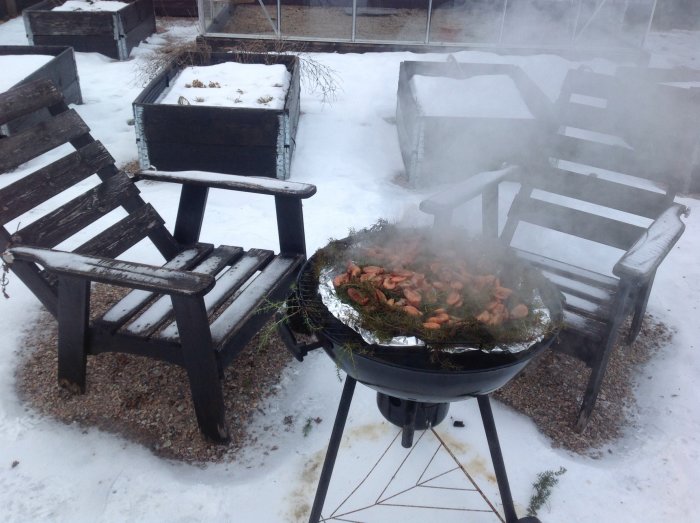 Rökning av räkor på grill i snöig trädgård med trädgårdsmöbler i bakgrunden.