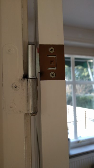 Närbild på en vit dörr och karm med gångjärn, tecken på att dörren kan vara kapat i botten.