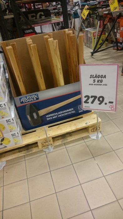 Säljskylt för 5 kg slägga med "hickory-stål" vid en hylla med hammarskaft i en bygghandel.