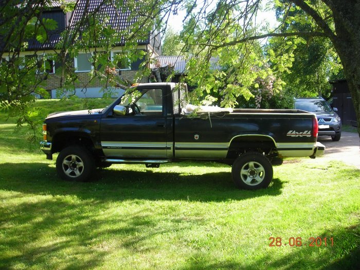 En svart och silverfärgad k2500 4wd pickup parkerad på gräs utomhus.