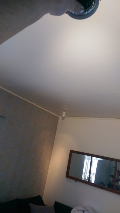 Person som håller en 3000k LED-ljuskälla med 2700k halogenlampa i taket i rummet.