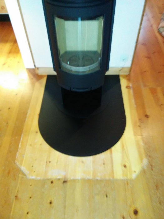 Nyinstallerad kamin på en rund svart platta med trägolv i bakgrunden.