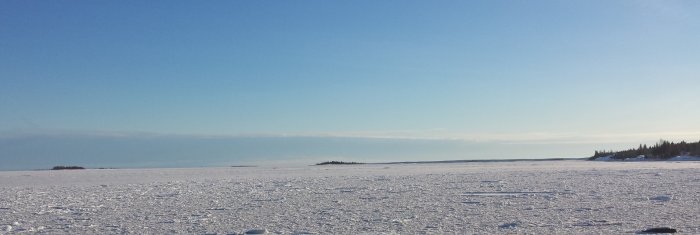 En frusen Bottenviken med snöklädd yta och klarblå himmel en solig förmiddag.