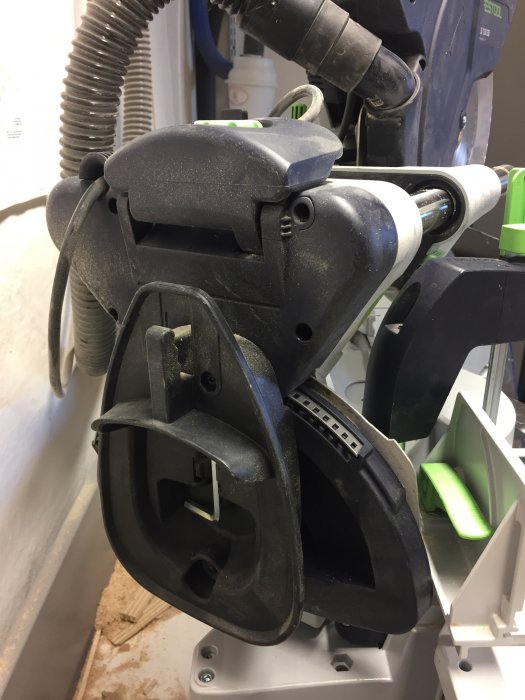 Närbild på borttagbart kabelgarage på en Festool sågmaskin, täckt med sågspån.