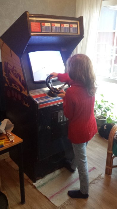 Barn spelar på en Atari Pole Position arkadspelmaskin i ett hemmamiljö.